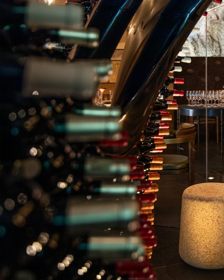 Wine bottles in the curved rack of the Ellerman House Wine Gallery, with the dining room beyond