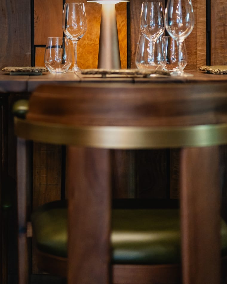 A table set with wine glasses and a small lamp against a wall of dark wood at Curate